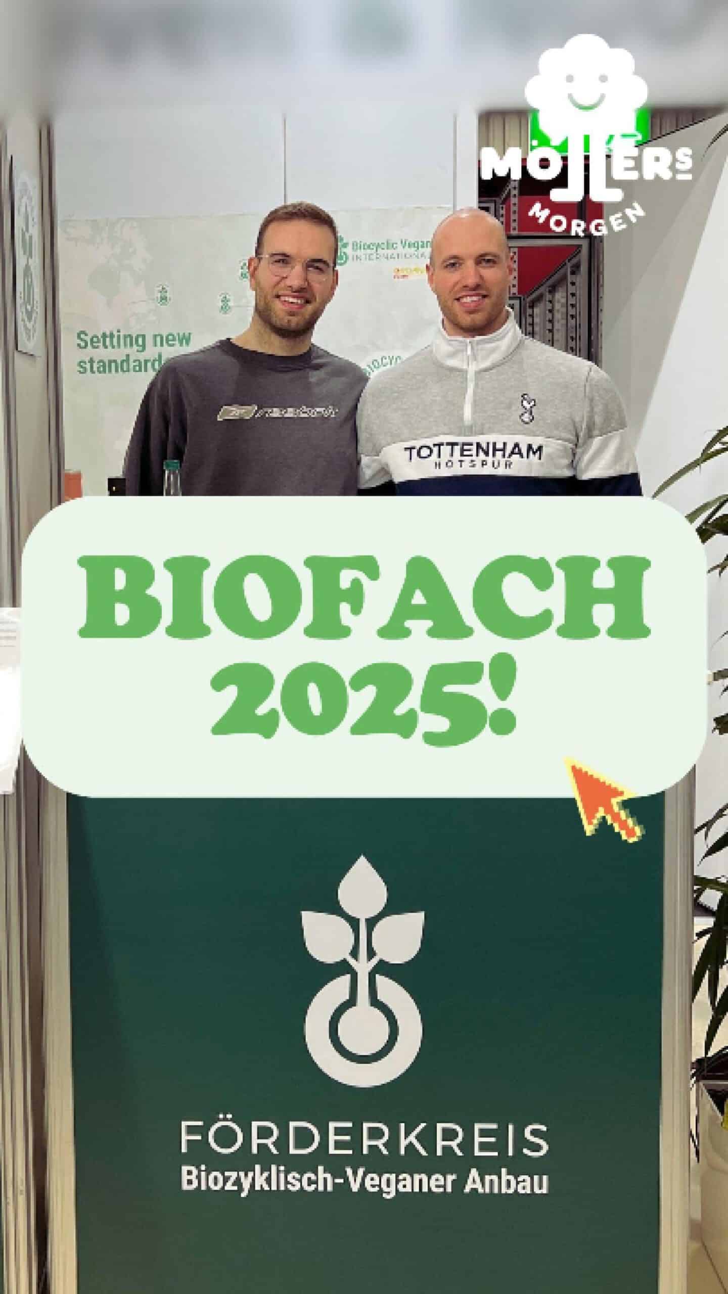 Zwei Personen stehen an einem Stand auf der Biofach 2025, während sie lächeln. Der Text „BIOFACH 2025!“ ist in grünen Buchstaben auf einem weißen Hintergrund zu sehen, zusammen mit einem Cursor-Pfeil. Der Stand gehört zum Förderkreis für biozyklisch-veganen Anbau, dessen Logo darunter zu sehen ist.